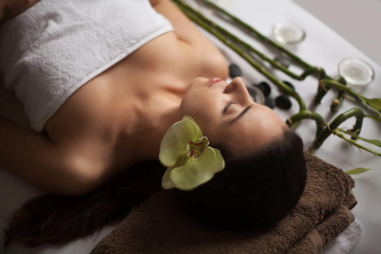A client relaxing during a facial at BEEs Day Spa in Coeur d'Alene, draped with a towel beside an orchid