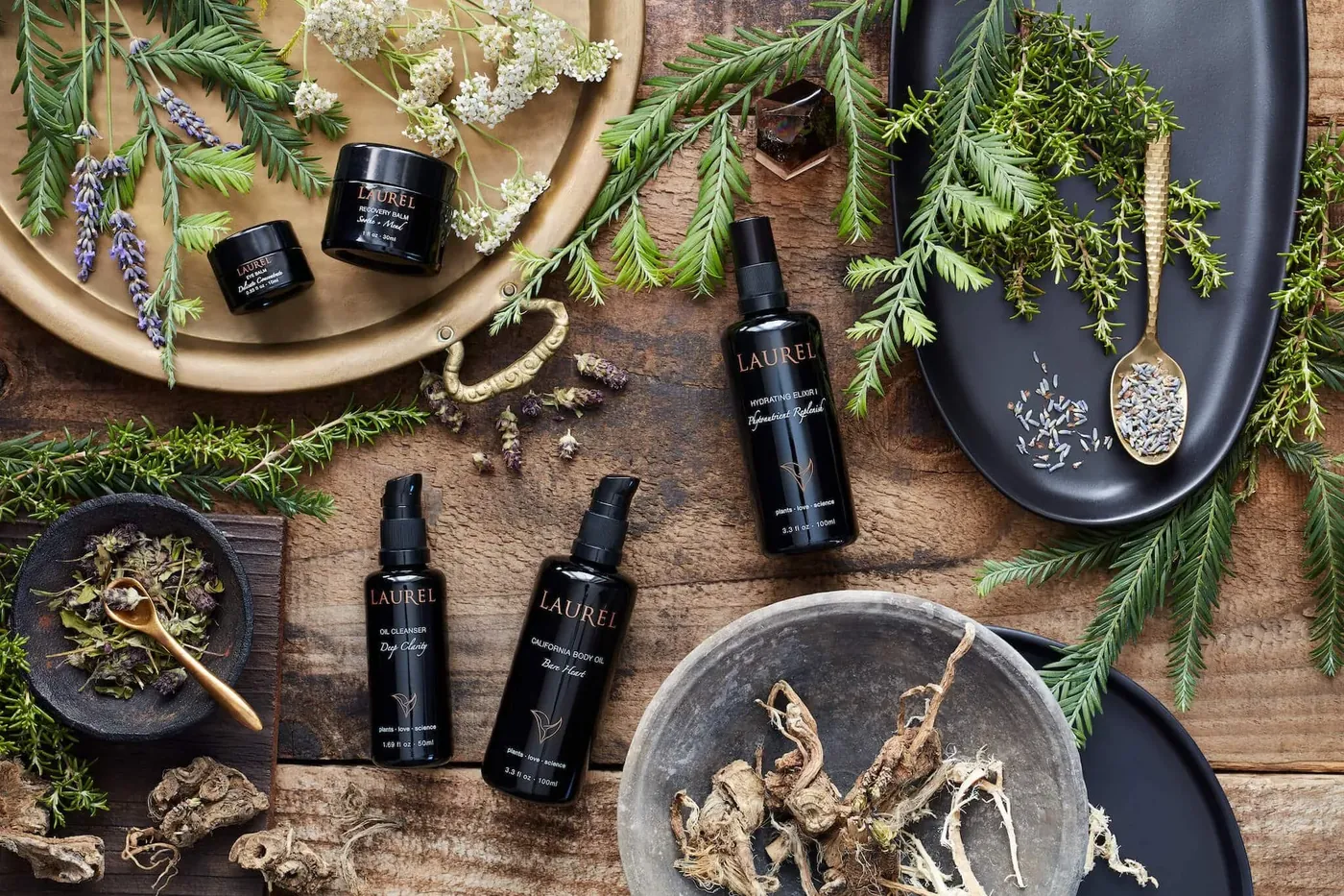Organic Laurel Skincare botanical products arranged with fresh herbs on a wood surface
